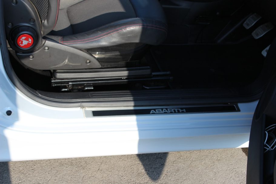 Close-up of a car door sill with a logo and partially shadowed interior.