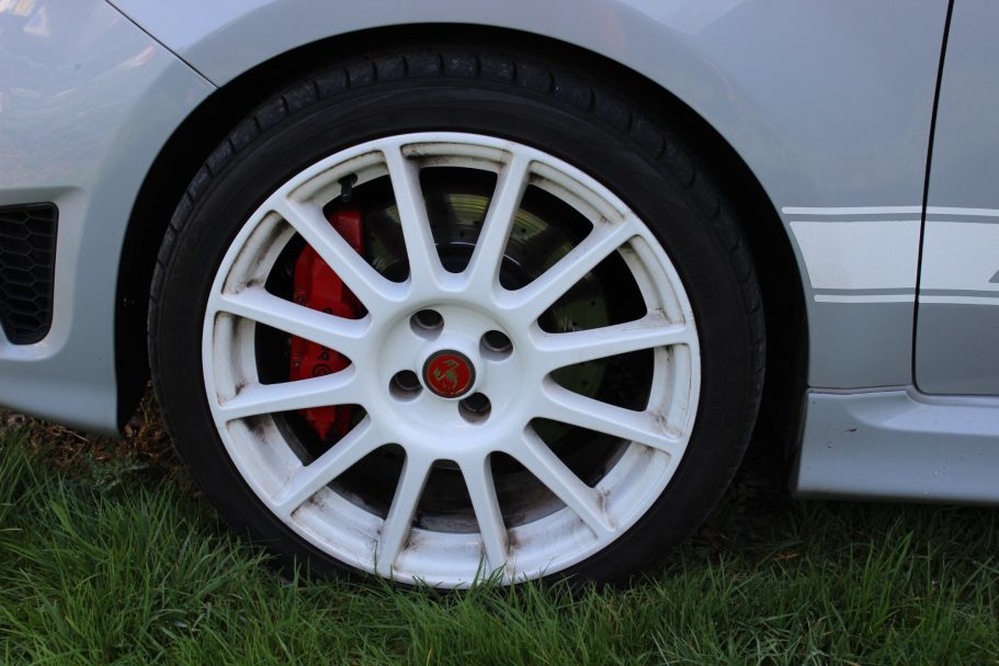 White alloy wheel with a red brake caliper, set against green grass.